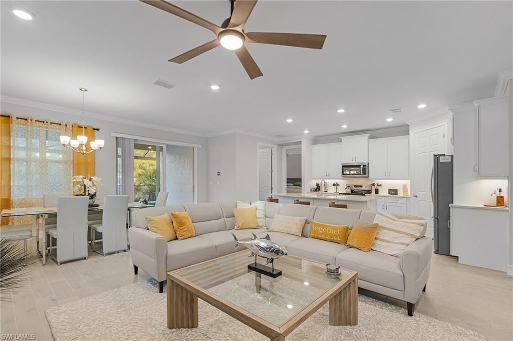 Living room with ceiling fan with notable chandelier, light wood-type flooring, and ornamental molding