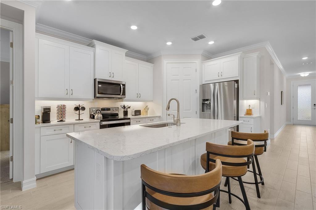 Kitchen with a center island with sink, sink, white cabinetry, and stainless steel appliances