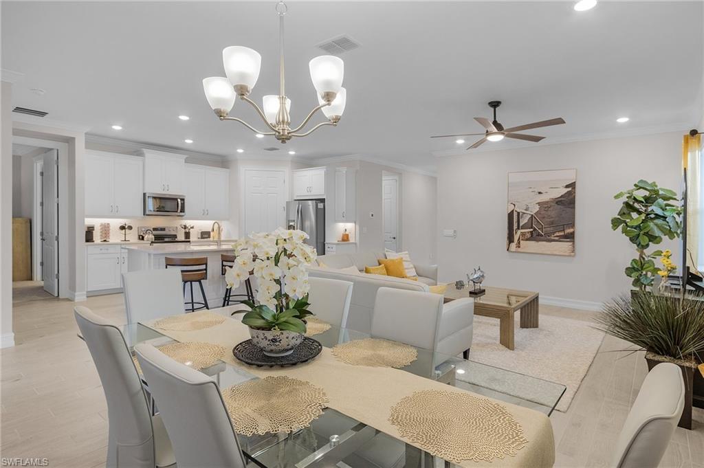 Dining area with crown molding, light hardwood / wood-style flooring, and ceiling fan with notable chandelier