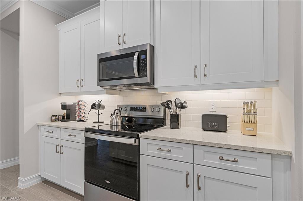 Kitchen featuring white cabinetry, tasteful backsplash, light stone counters, crown molding, and appliances with stainless steel finishes