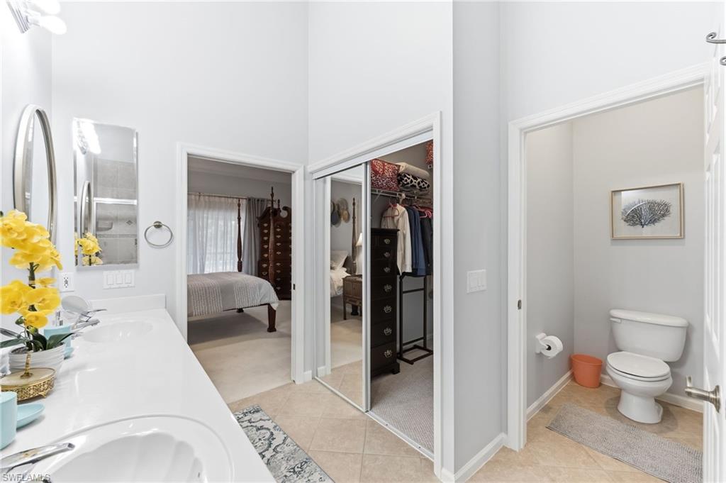 Ensuite bathroom with double vanity, a high ceiling, light tile patterned flooring, and a walk in closet
