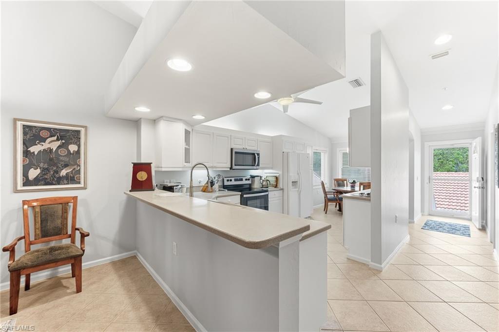 Kitchen with stainless steel appliances, a peninsula, light countertops, white cabinets, and vaulted ceiling