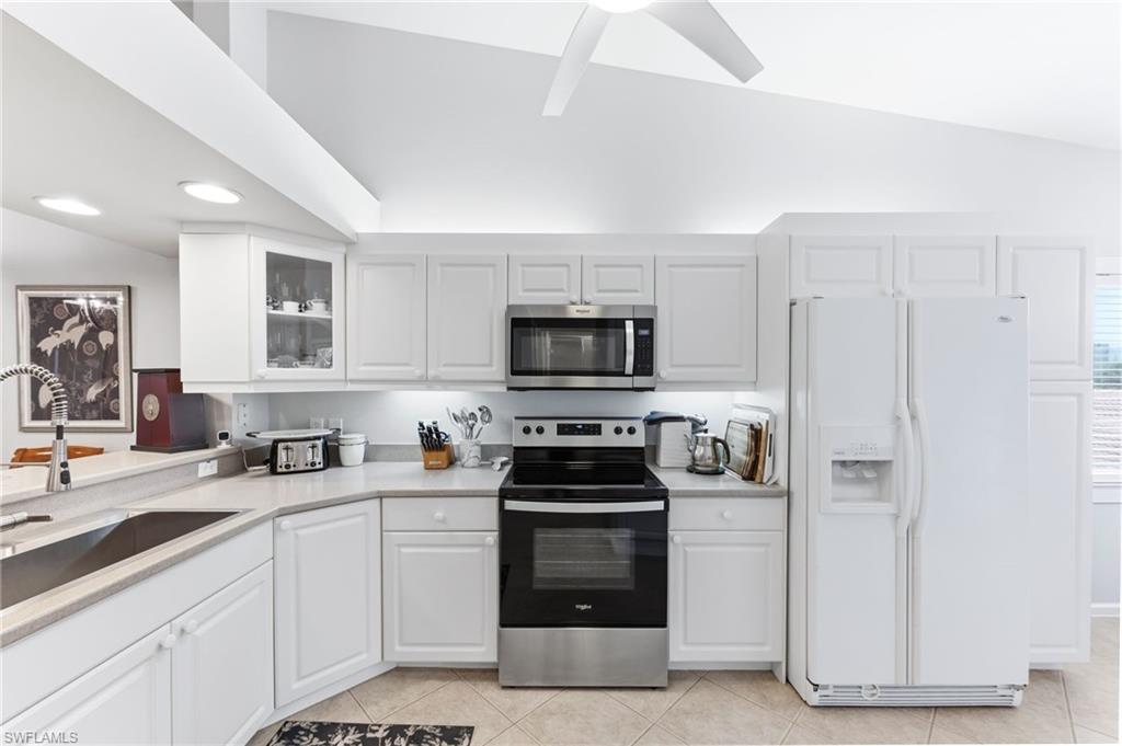 Kitchen with stainless steel appliances, lofted ceiling, white cabinets, glass fronted cabinets, and a ceiling fan