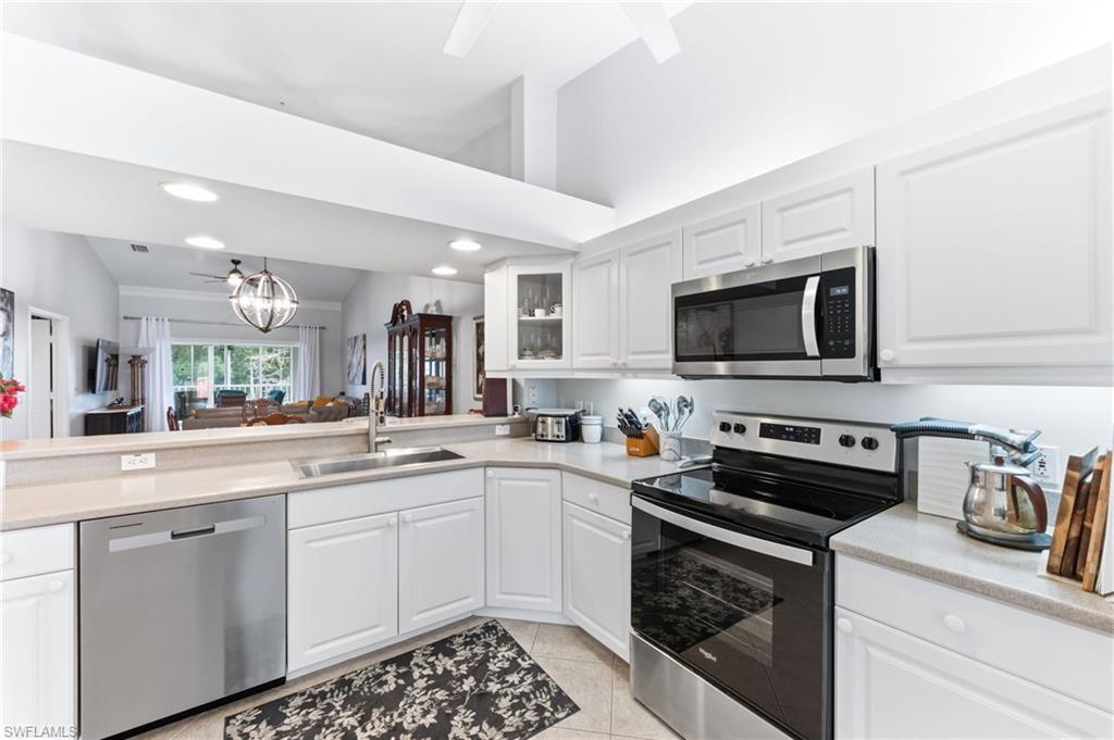 Kitchen with stainless steel appliances, white cabinets, vaulted ceiling, hanging lights, and glass fronted cabinets