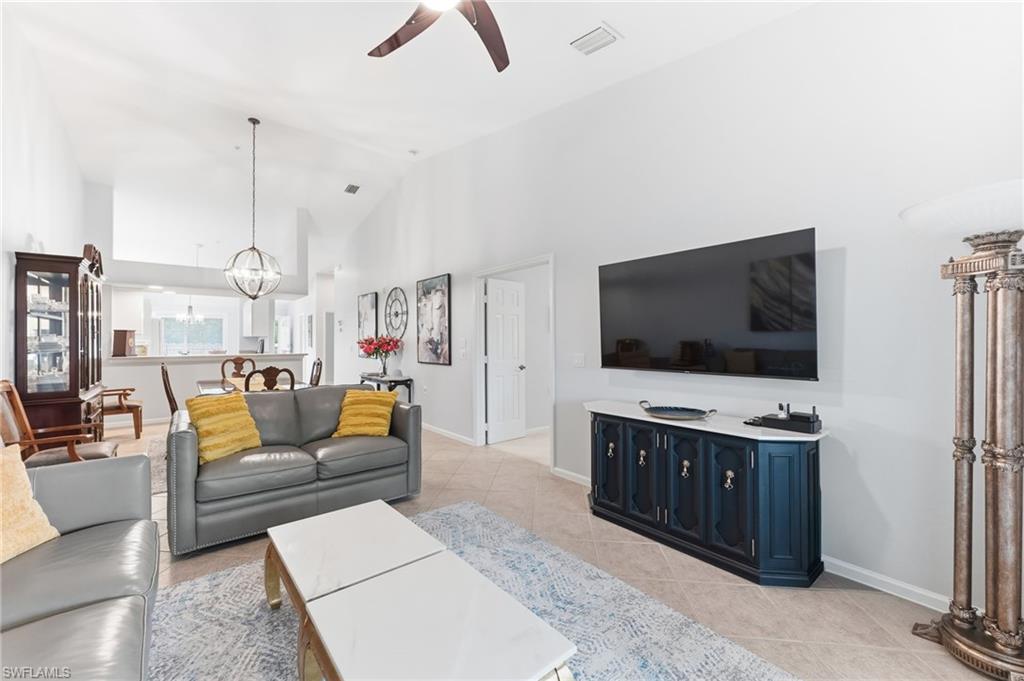 Living room with hanging lights, ceiling fan, light tile patterned floors, and lofted ceiling