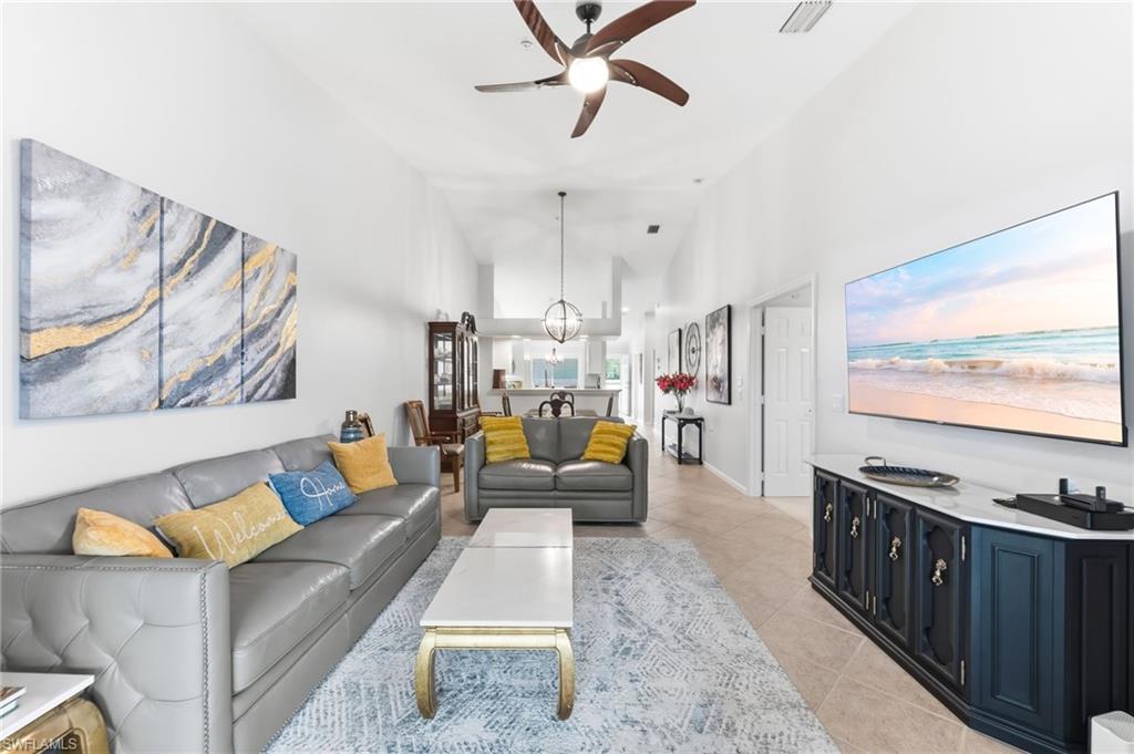 Living room with ceiling fan, light tile patterned floors, and lofted ceiling