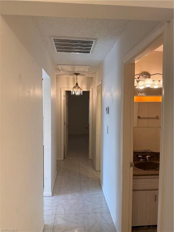 Corridor featuring a textured ceiling and a chandelier