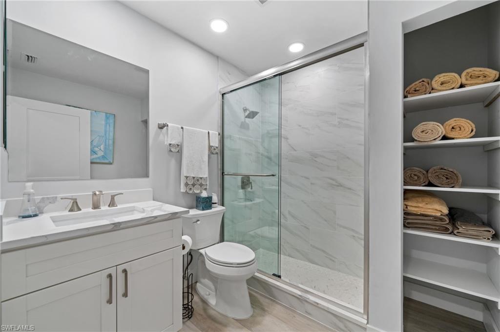 Bathroom with vanity, a marble finish shower, light wood-type flooring, and recessed lighting