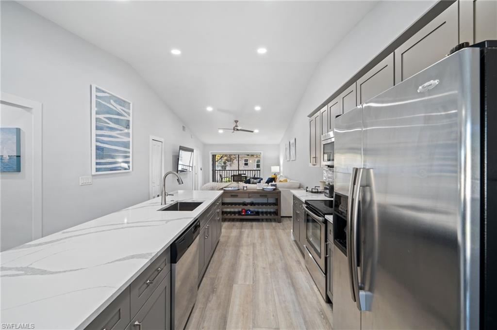 Kitchen featuring stainless steel appliances, gray cabinets, lofted ceiling, open floor plan, and light wood finished floors