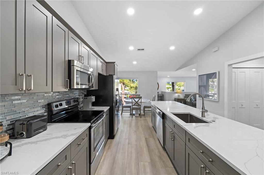 Kitchen featuring gray cabinetry, stainless steel appliances, vaulted ceiling, light stone counters, and light wood-style flooring