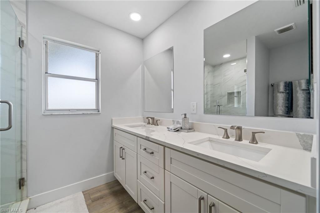 Full bath with double vanity, a marble finish shower, light wood-type flooring, and recessed lighting