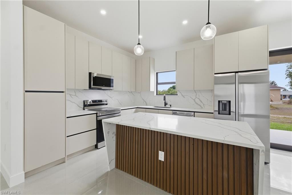 Kitchen featuring a center island, stainless steel appliances, light stone counters, hanging light fixtures, and modern cabinets
