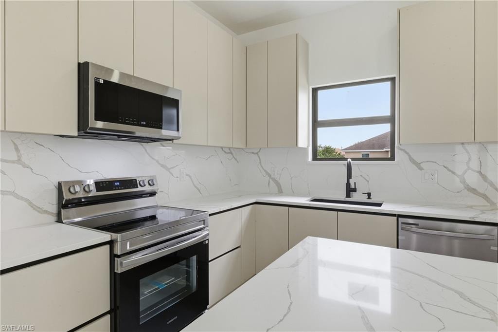 Kitchen featuring stainless steel appliances, light stone counters, decorative backsplash, and modern cabinets