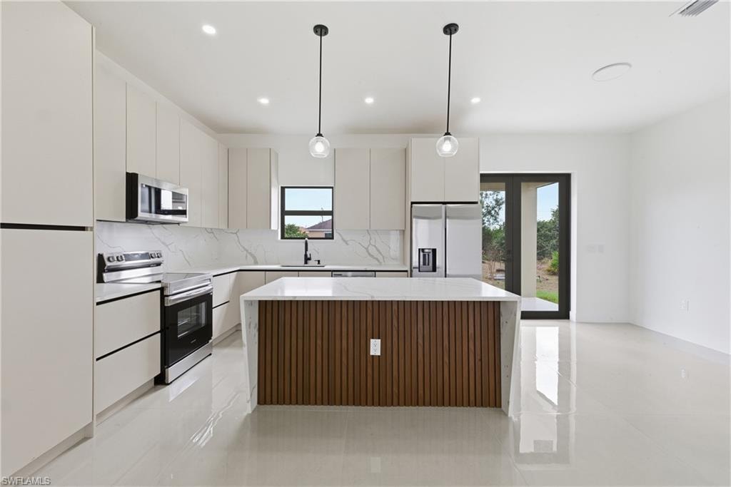 Kitchen with a kitchen island, stainless steel appliances, hanging light fixtures, and light tile patterned floors