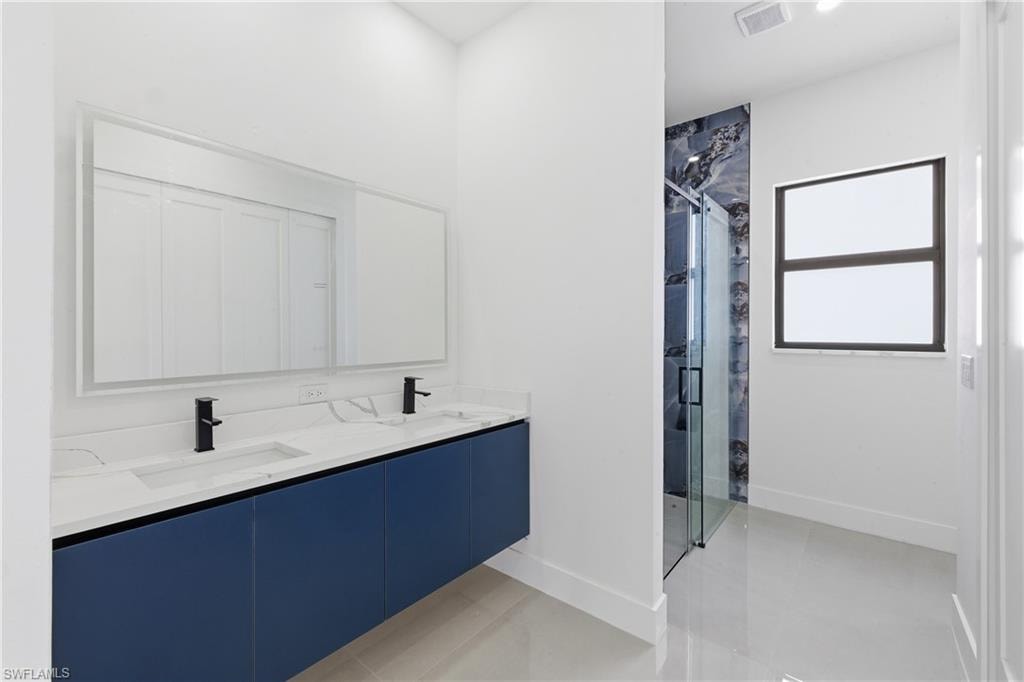 Full bath with a marble finish shower, double vanity, and light tile patterned floors
