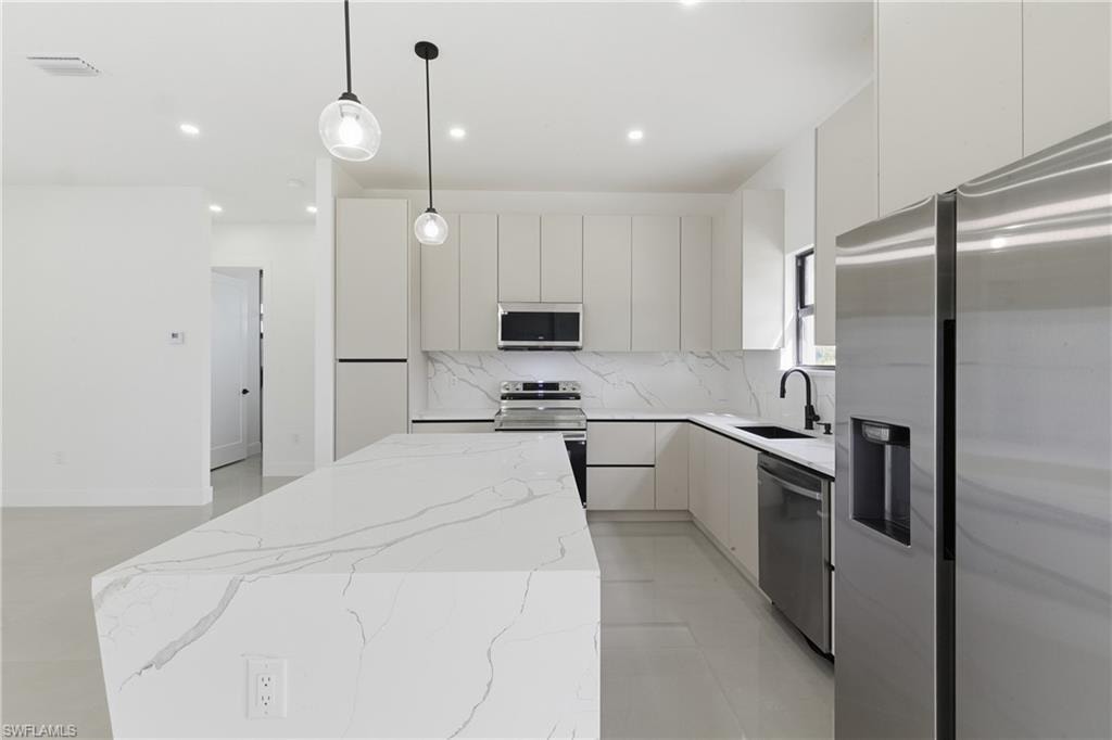 Kitchen with stainless steel appliances, modern cabinets, light stone countertops, a kitchen island, and hanging light fixtures