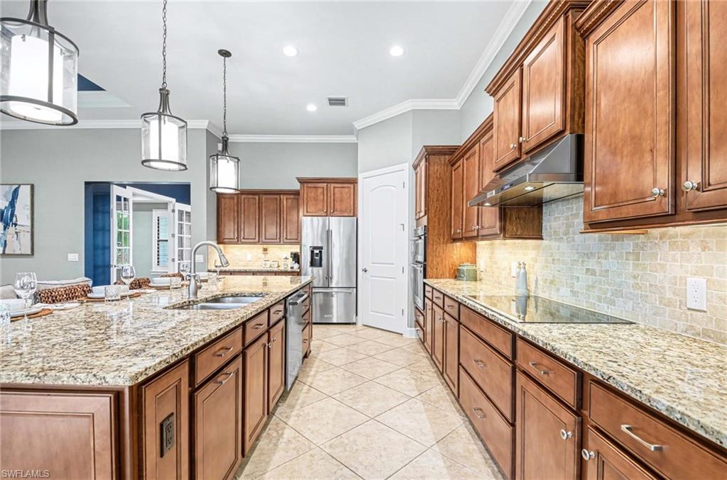 Kitchen with wood finish cabinets, light stone countertops, crown molding, stainless steel appliances, and pendant lighting