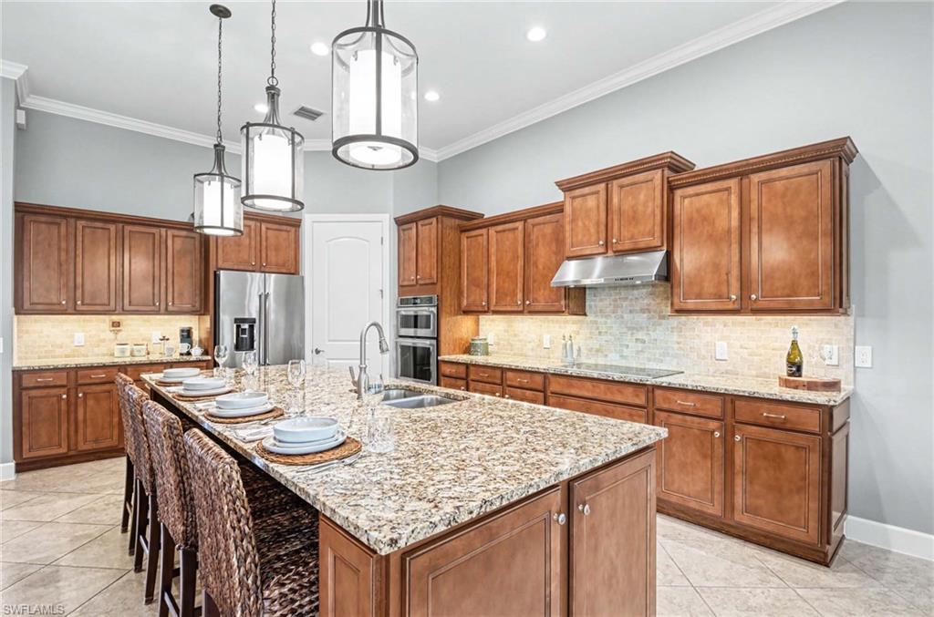 Kitchen with wood finish cabinetry, light stone countertops, a breakfast bar, stainless steel appliances, and hanging light fixtures