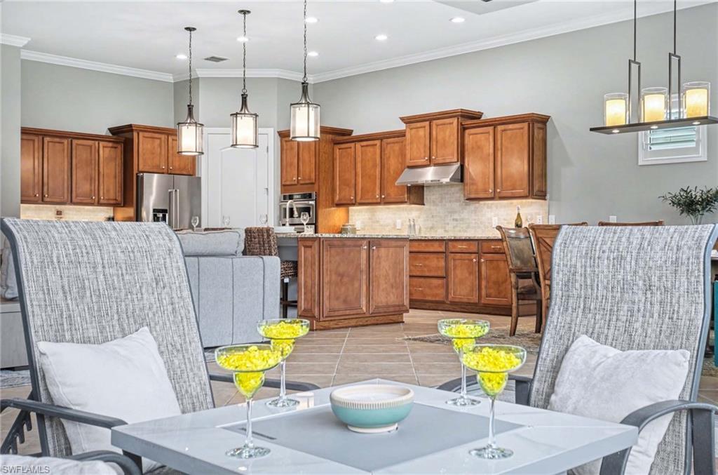 Kitchen featuring wood finish cabinets, stainless steel appliances, light tile patterned flooring, pendant lighting, and ornamental molding