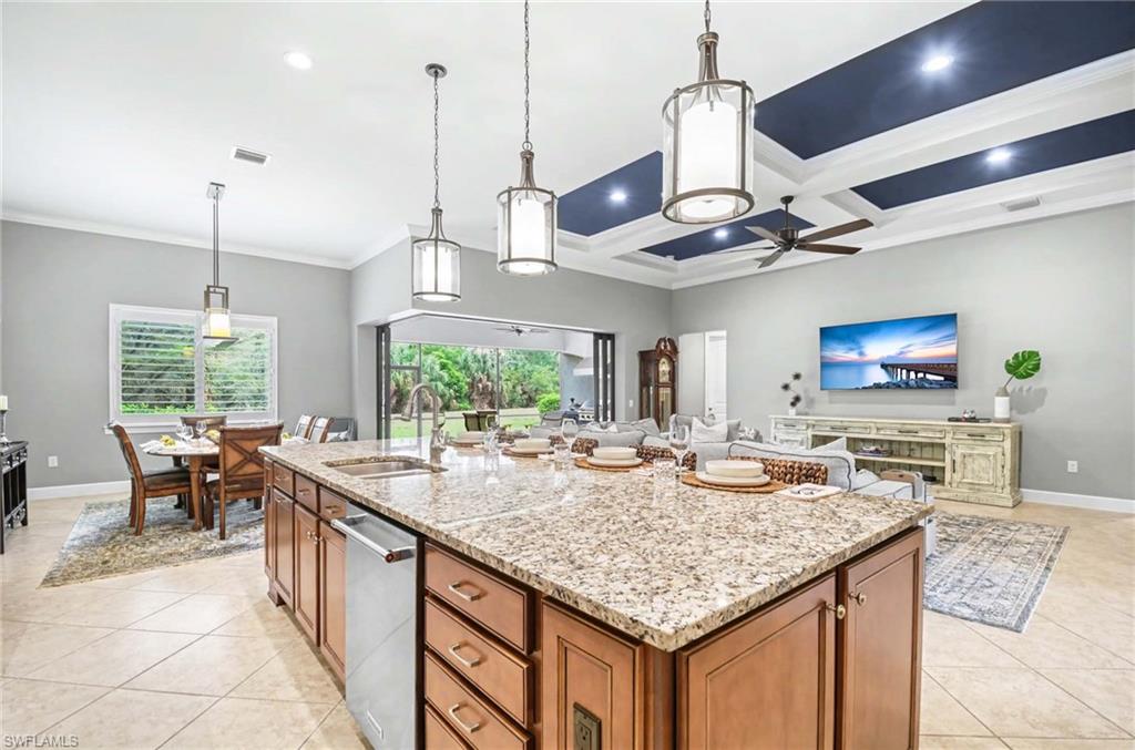 Kitchen with light stone counters, an island with sink, pendant lighting, open floor plan, and coffered ceiling