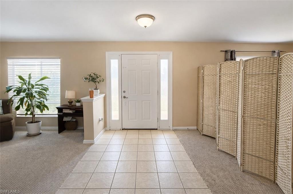 Entryway with light colored carpet and light tile patterned flooring