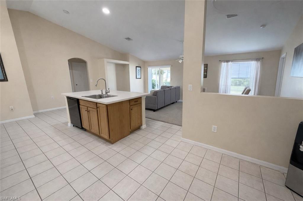 Kitchen featuring lofted ceiling, a kitchen island with sink, light countertops, open floor plan, and arched walkways