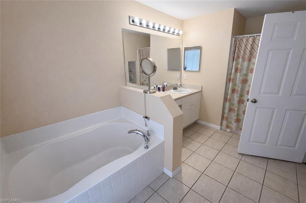 Bathroom featuring vanity, a shower with curtain, light tile patterned floors, and a garden tub