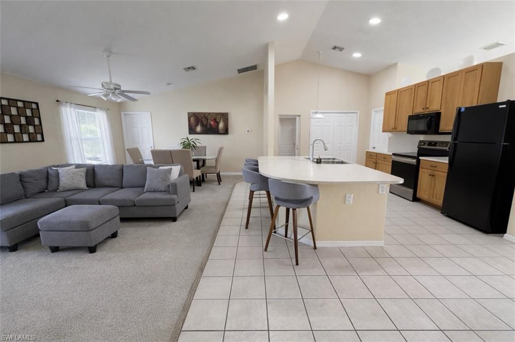 Kitchen featuring open floor plan, black appliances, light countertops, an island with sink, and a breakfast bar area