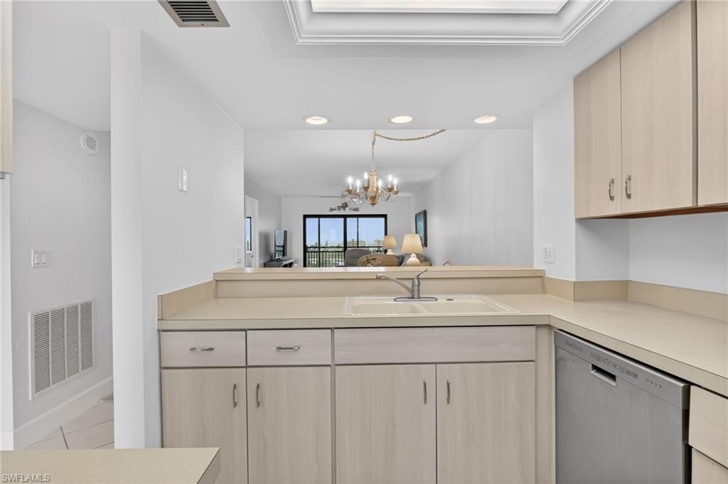 Kitchen with light countertops, stainless steel dishwasher, light wood finish cabinets, a chandelier, and open floor plan
