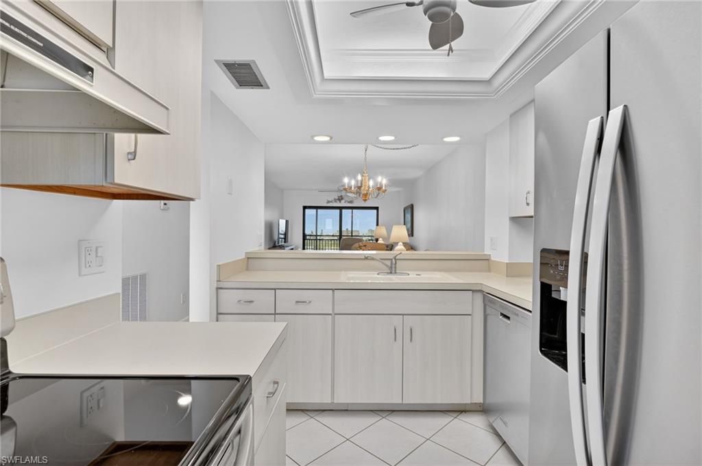 Kitchen with stainless steel appliances, light countertops, hanging lights, a tray ceiling, and light tile patterned flooring