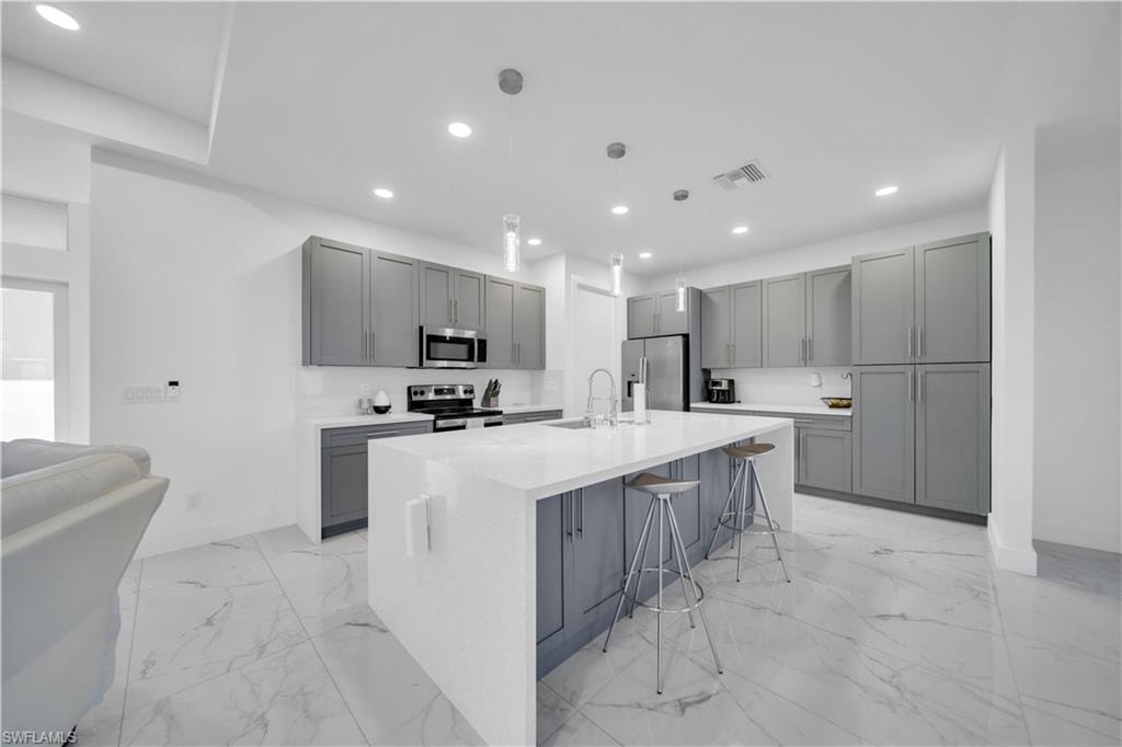 Kitchen featuring gray cabinets, a breakfast bar area, an island with sink, light stone counters, and stainless steel appliances