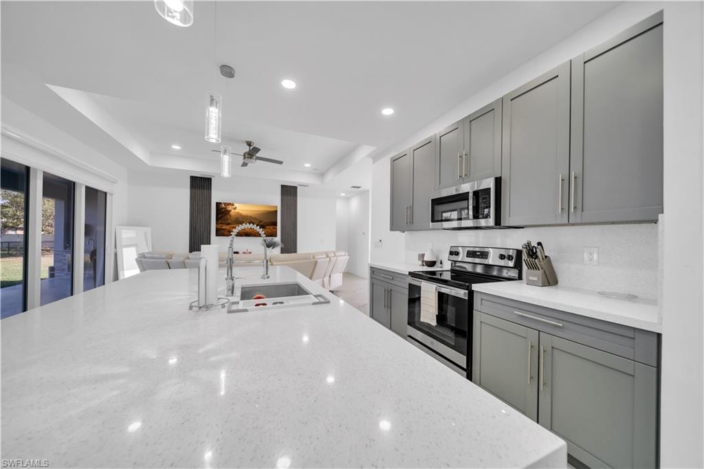 Kitchen featuring stainless steel appliances, light stone counters, pendant lighting, ceiling fan, and a tray ceiling