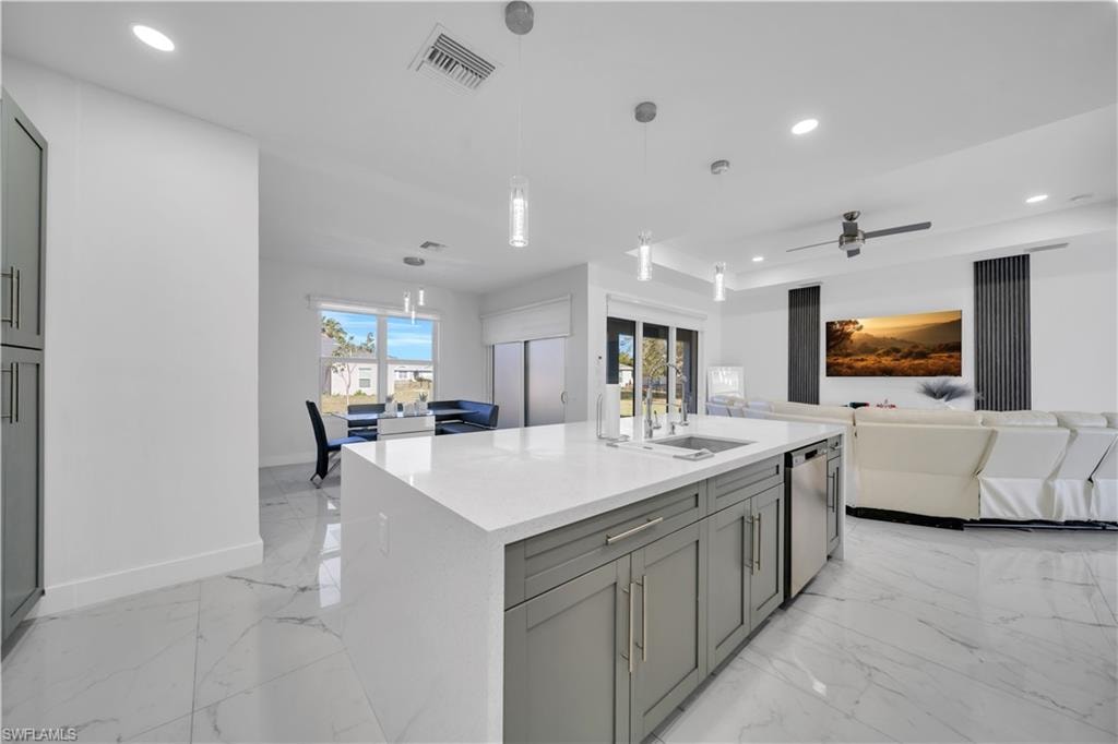 Kitchen with gray cabinetry, a center island with sink, light stone countertops, open floor plan, and pendant lighting