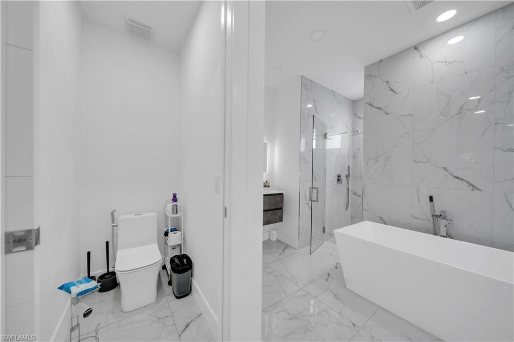 Full bathroom with vanity, a marble finish shower, a freestanding tub, recessed lighting, and light marble finish floors
