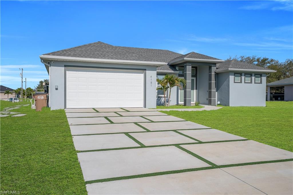 Prairie-style home with a front yard, stucco siding, a shingled roof, and concrete driveway