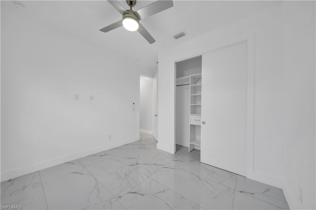 Unfurnished bedroom featuring light marble finish floors, a ceiling fan, and a closet