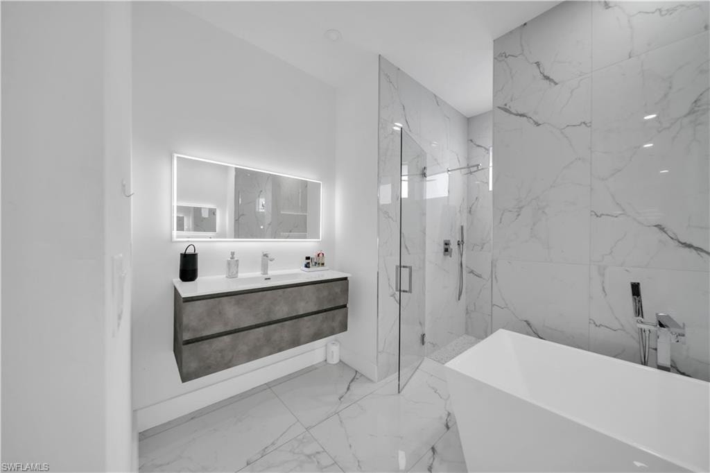 Full bathroom with a marble finish shower, a soaking tub, vanity, and light marble finish floors