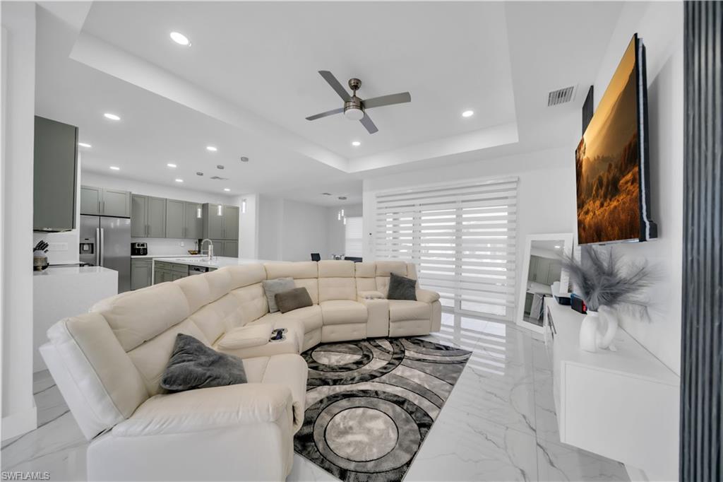 Living room featuring a ceiling fan, light marble finish flooring, a raised ceiling, and recessed lighting