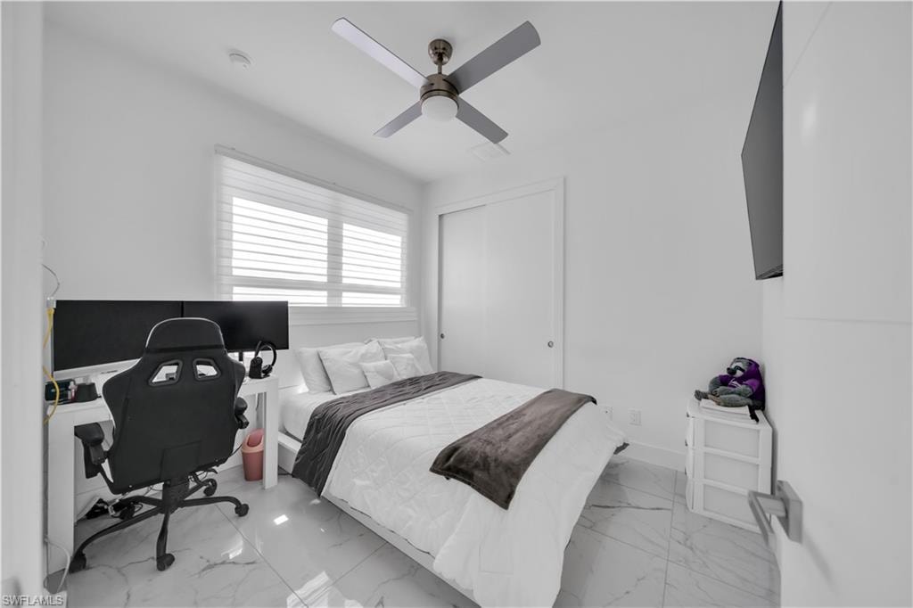 Bedroom featuring a desk, ceiling fan, a closet, and light marble finish flooring