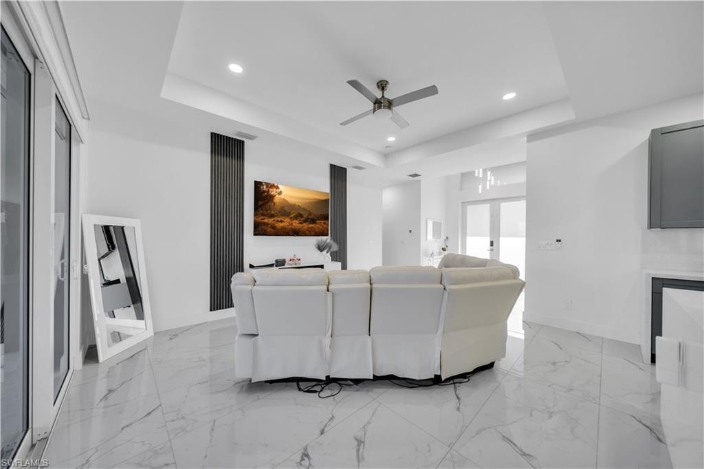 Cinema featuring a ceiling fan, a raised ceiling, recessed lighting, light marble finish flooring, and french doors
