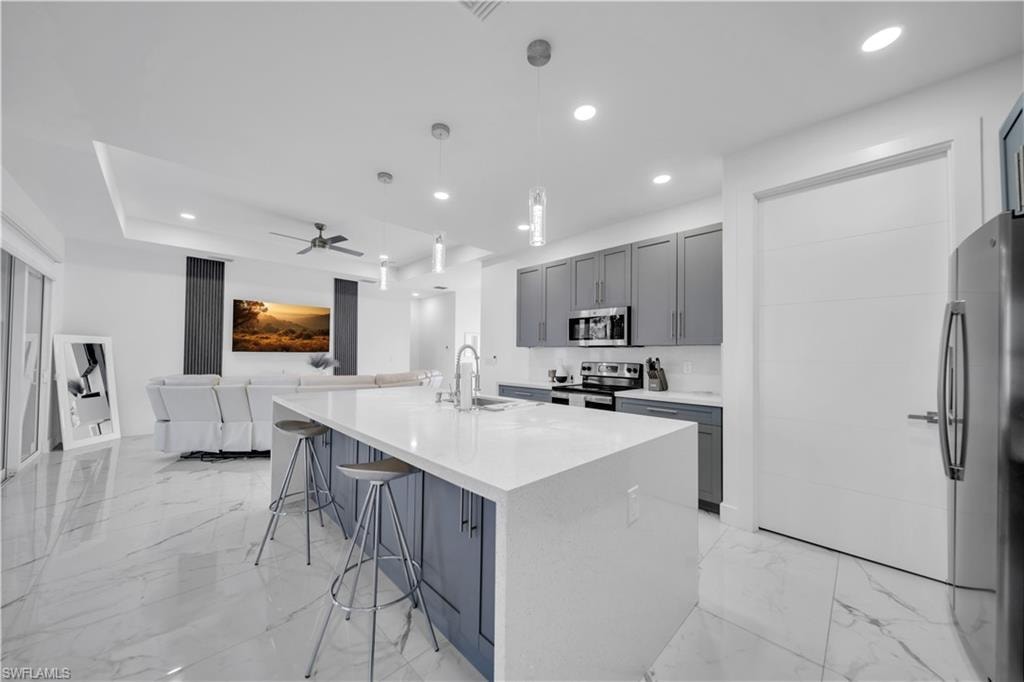 Kitchen featuring gray cabinets, a breakfast bar, light stone countertops, and a spacious island