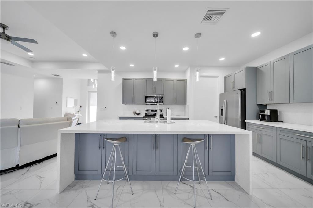 Kitchen with gray cabinets, light stone countertops, a large island, and stainless steel appliances