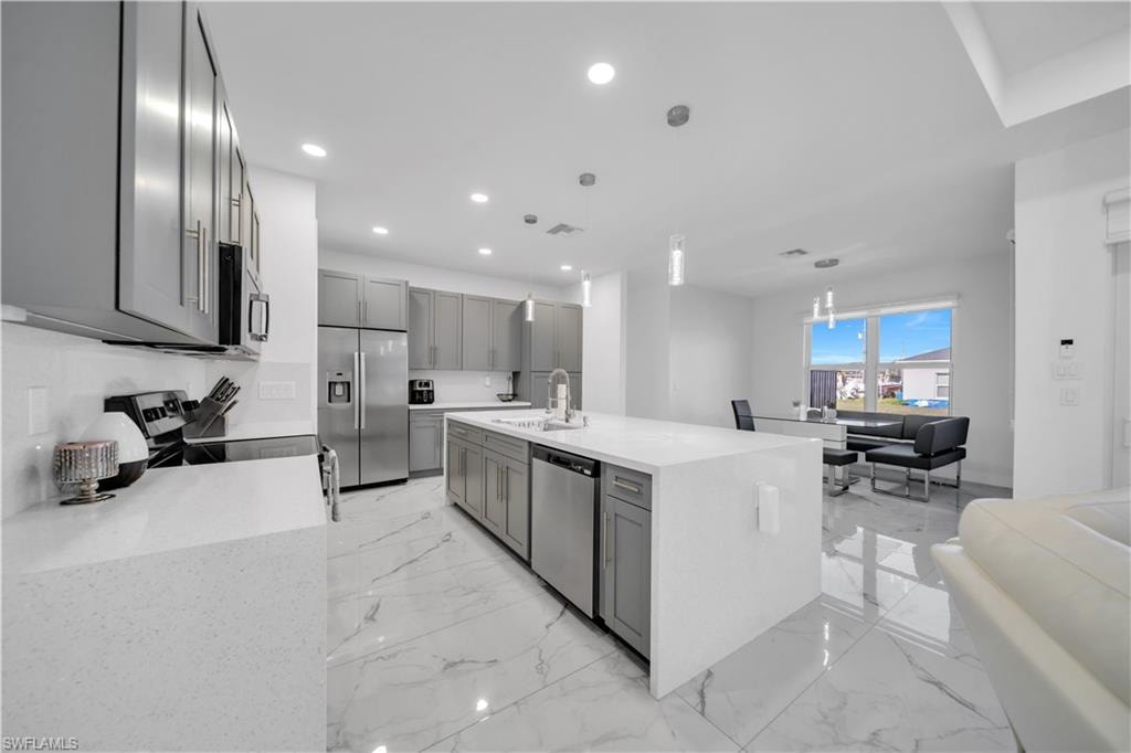 Kitchen with gray cabinetry, light stone countertops, stainless steel appliances, and open floor plan