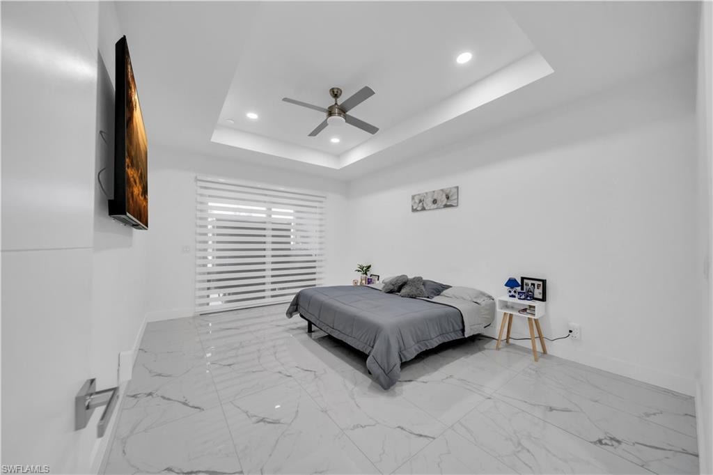Bedroom with recessed lighting, light marble finish flooring, ceiling fan, and a raised ceiling