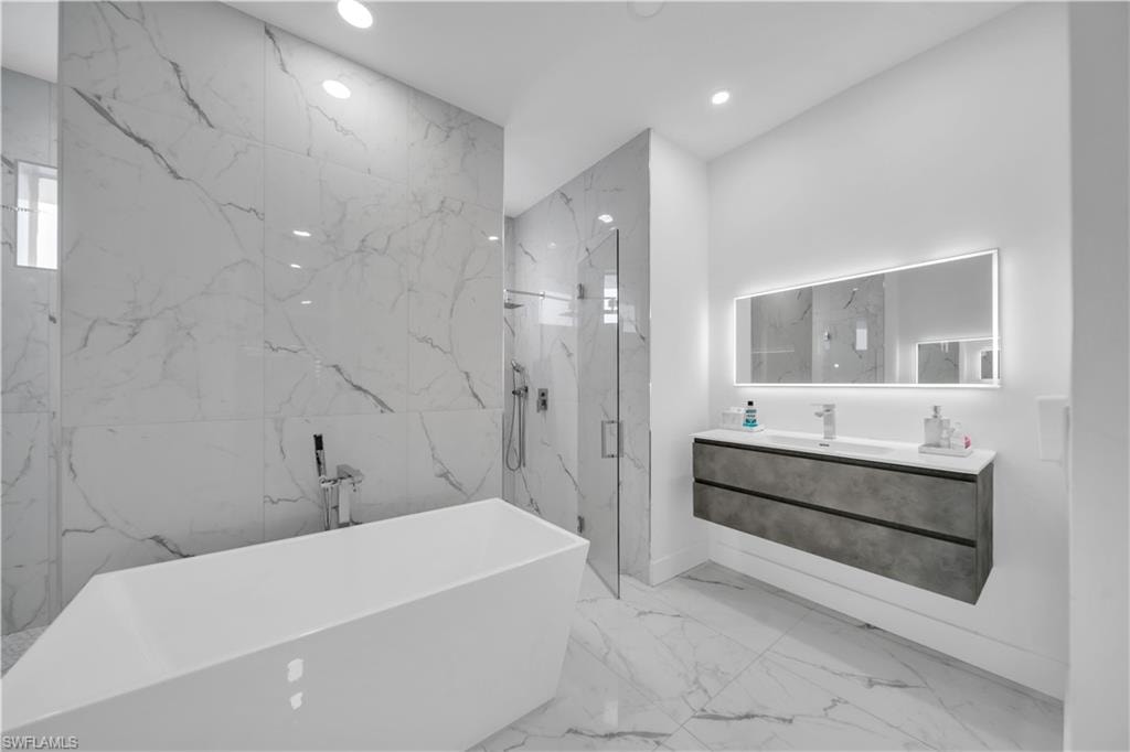 Bathroom with a marble finish shower, a freestanding tub, vanity, stone wall, and recessed lighting