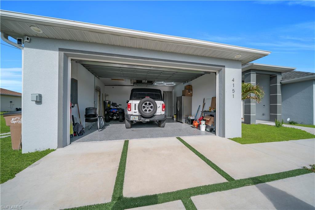 Garage featuring freestanding refrigerator, concrete driveway, and electric panel