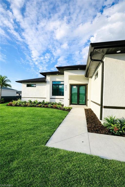 View of exterior entry featuring stucco ,siding, a lawn, and french doors-reel color grass