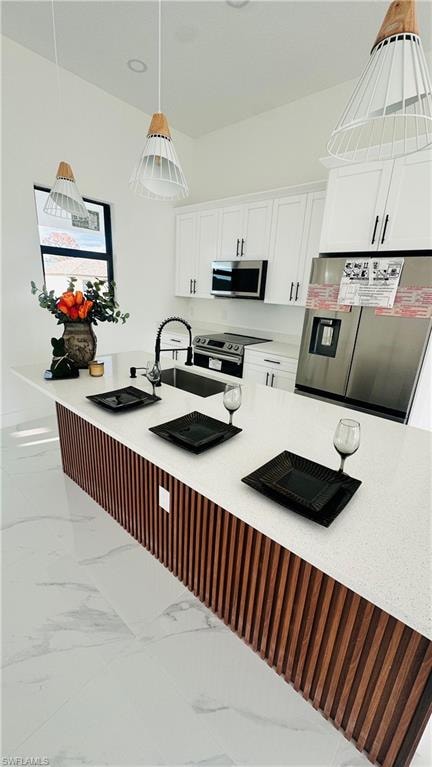Kitchen with stainless steel appliances, white cabinets, a breakfast bar area, light stone counters, and hanging light fixtures