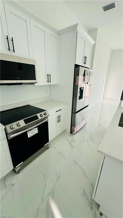 Kitchen with stainless steel appliances, white cabinetry, light marble finish floors, and light stone countertops