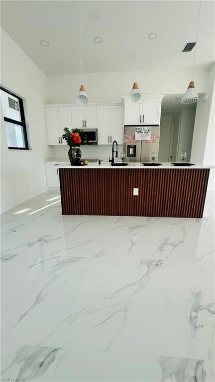 Kitchen with pendant lighting, stainless steel appliances, a center island with sink, two tone color scheme, and light stone counters